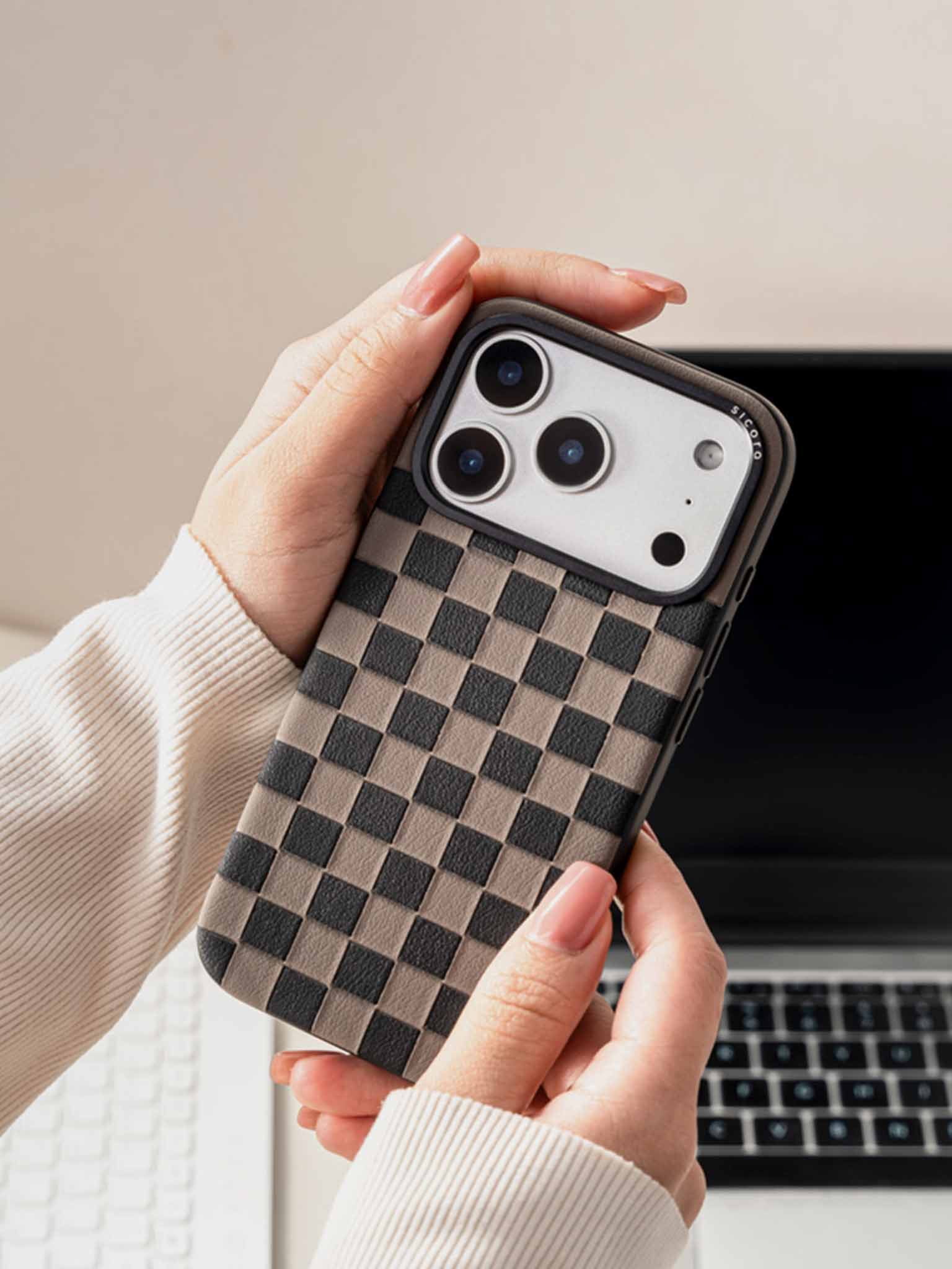 A woman holding sicora checkerboard phone case with black and granite gray checkered pattern in front of a laptop