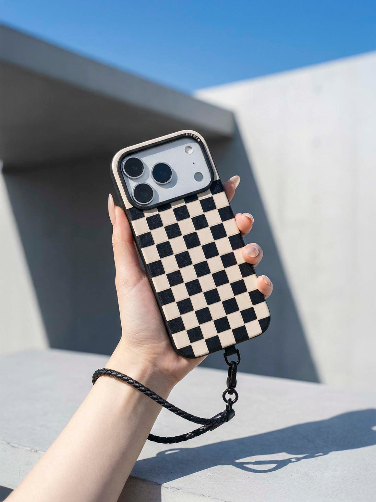 Hand holding a sicora checkerboard phone case against a modern architectural background