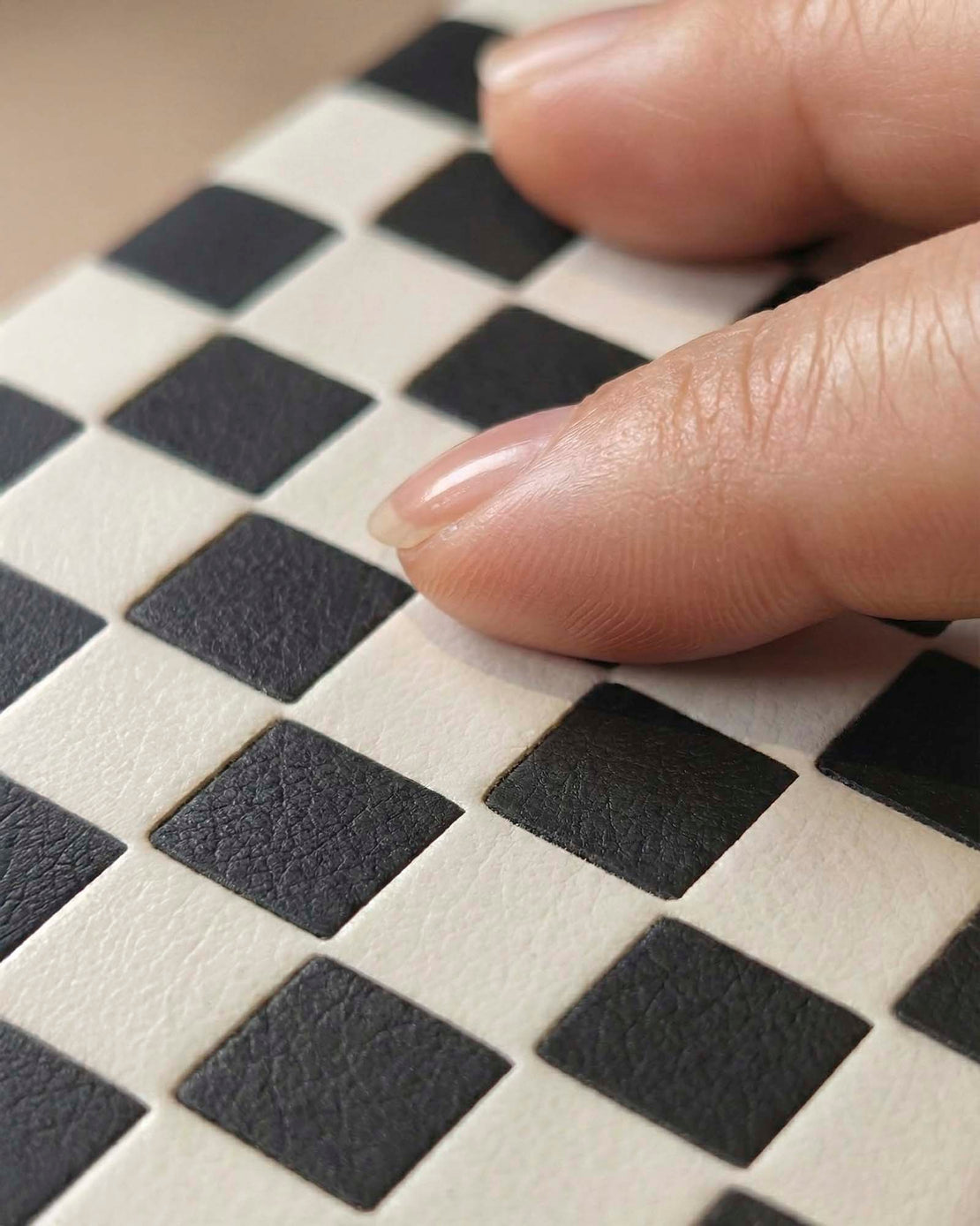 Close-up of a hand touching a silio leather black and white woven checkered surface.