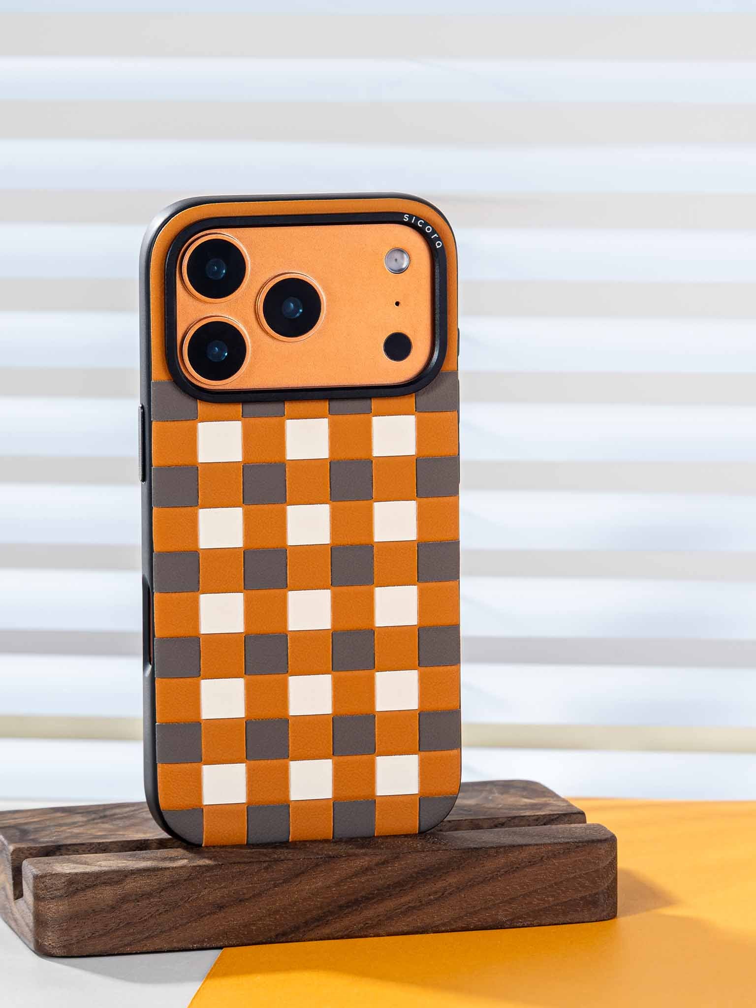 Sicora checkerboard phone case with toffee gold, granite gray and cream white checkered pattern on a wooden stand