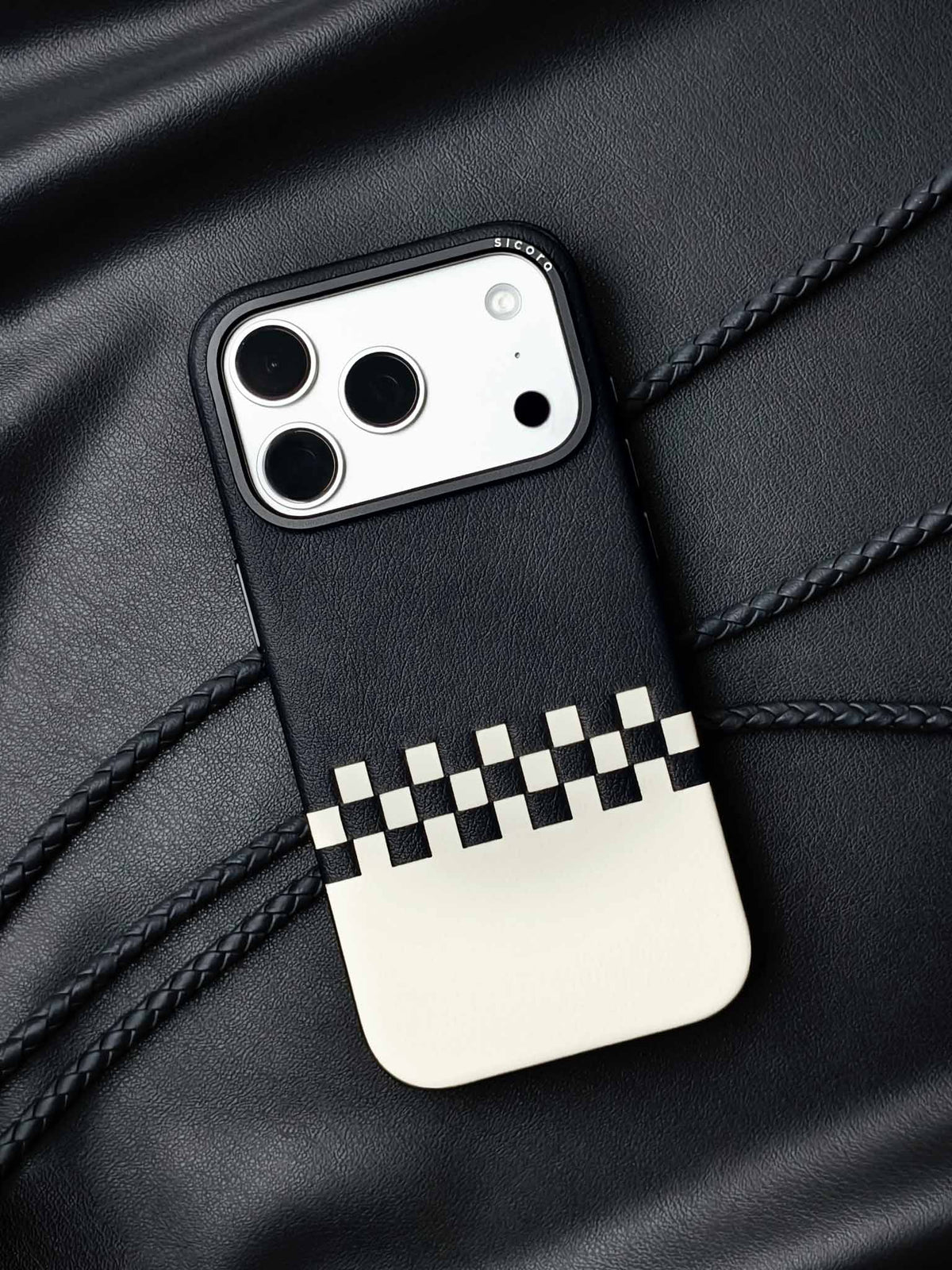 sicora iPhone 18 pro / iPhone 17 pro vegan leather phone case, crossover case featuring a black and cream hand-woven leather color blocking pattern, braided phone lanyards and black leather background