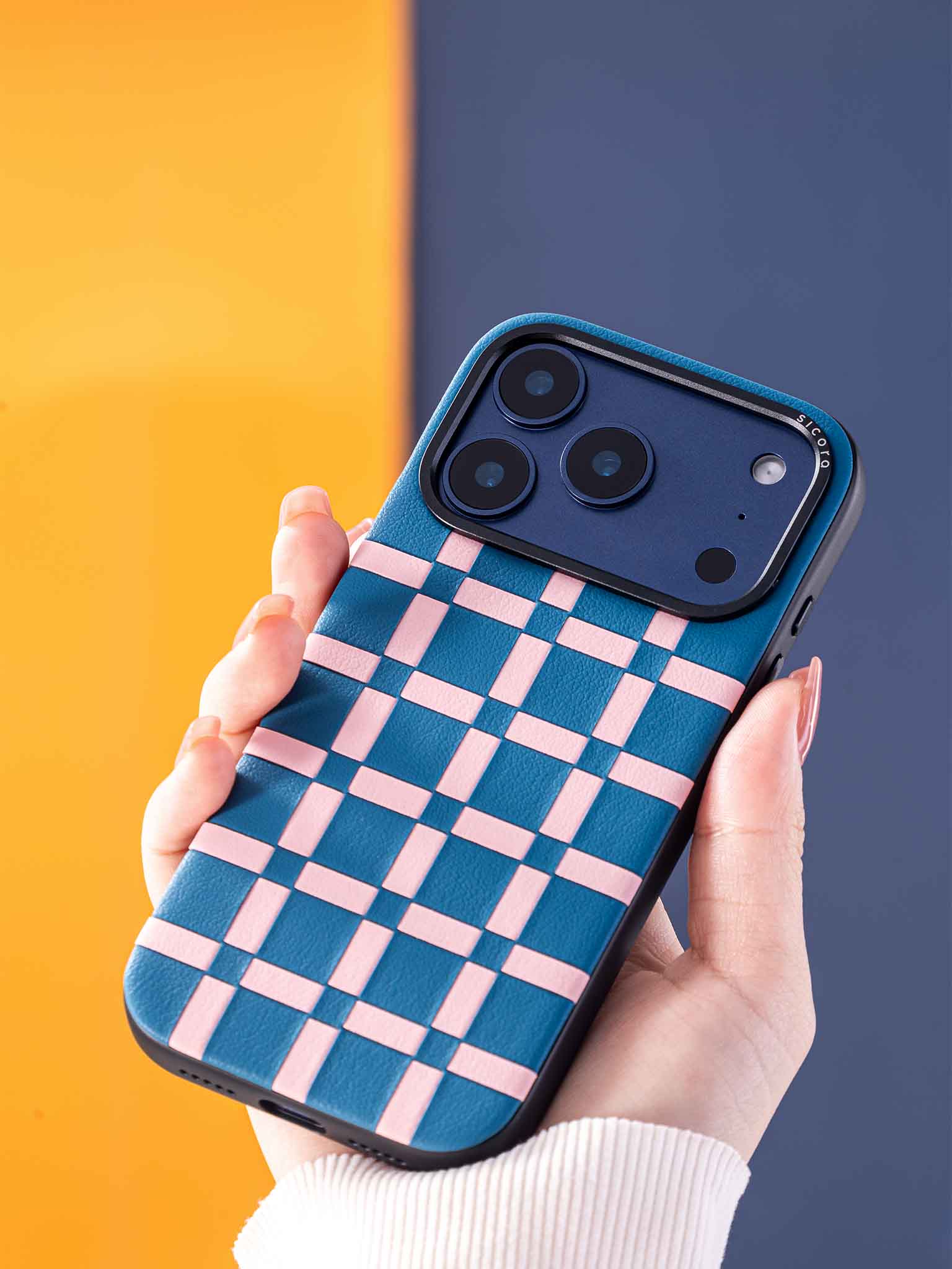 Sicora gridplay phone case with sea blue and pink checkered pattern held by a hand against a colorful background