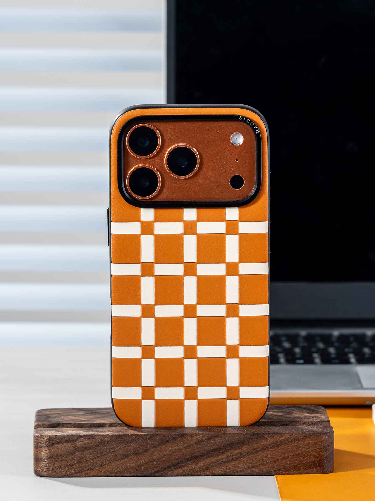 Sicora gridplay phone case with toffee gold and cream white checkered pattern on a wooden stand in front of a laptop