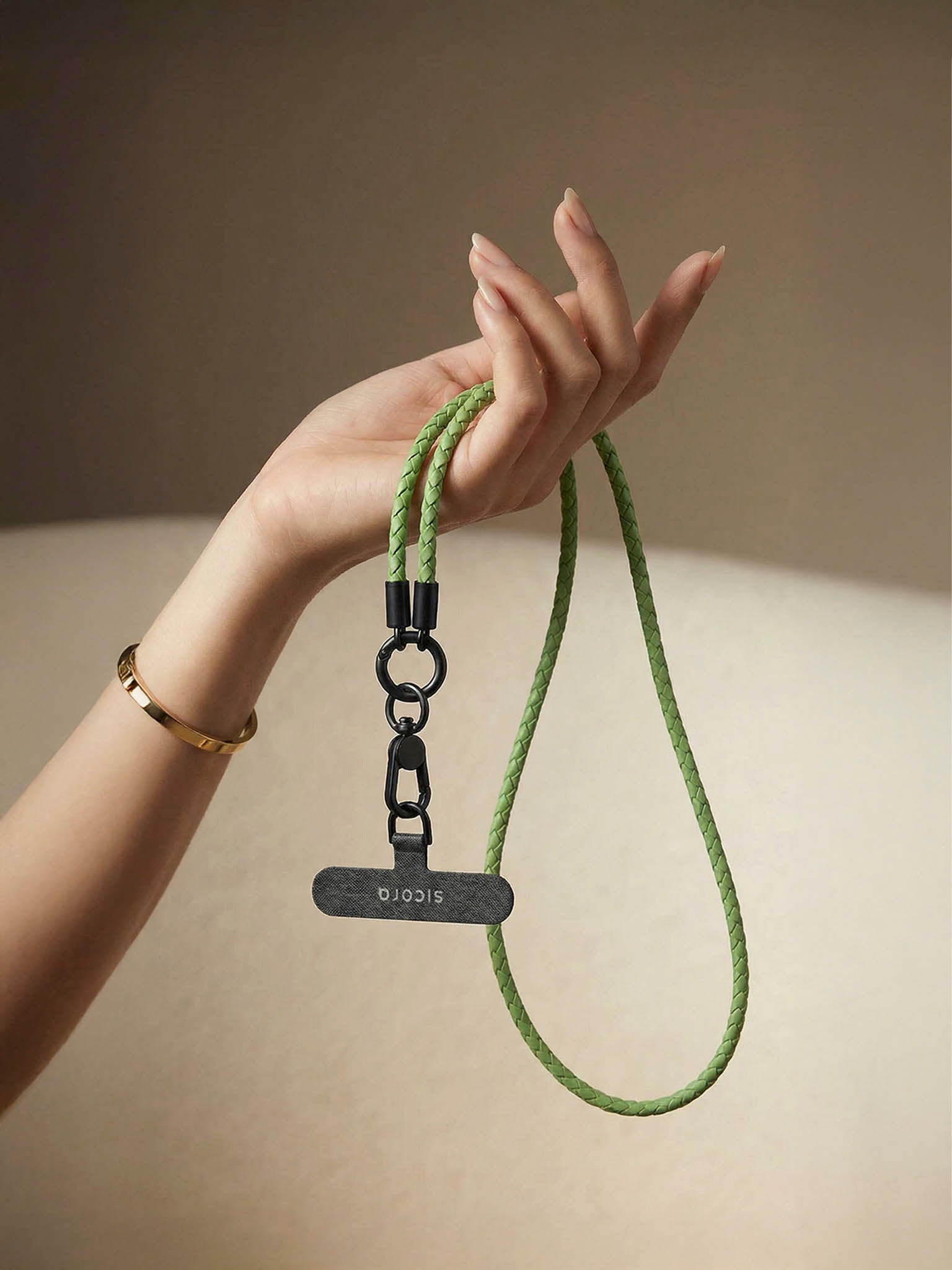 Hand holding a sicora green lanyard with a black tag against a neutral background