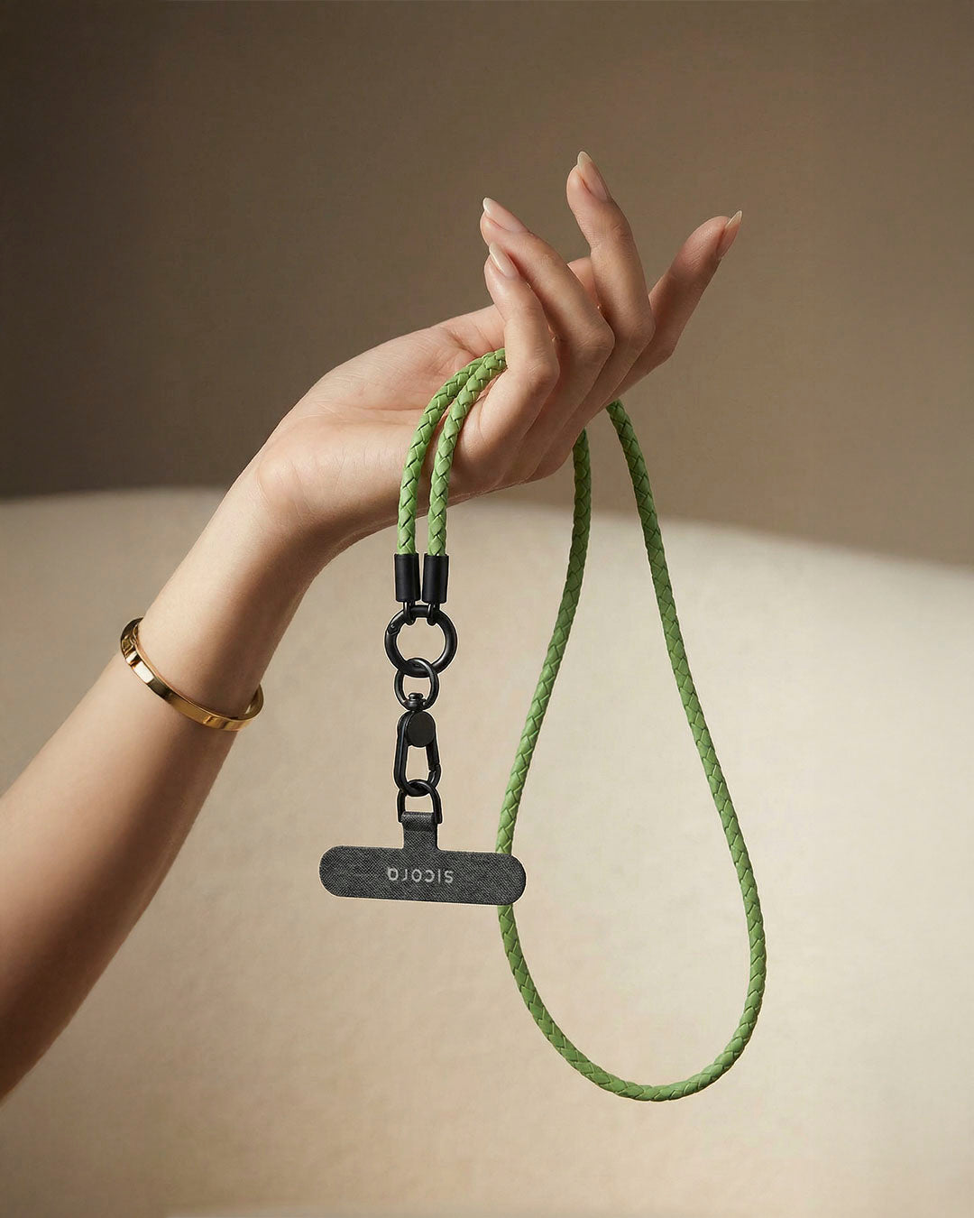 Hand holding a sicora green leather loop lanyard with a black tag against a neutral background