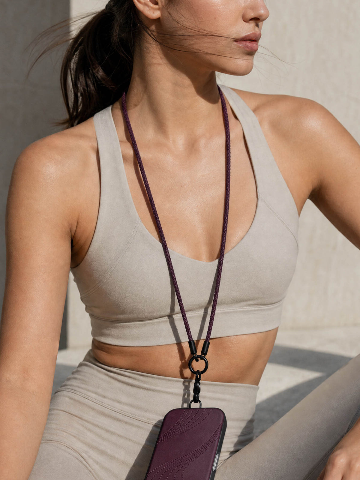 A woman wearing a sicora dark cherry purple braided leather cord / loop phone lanyard with a matching purple flow case iphone case.