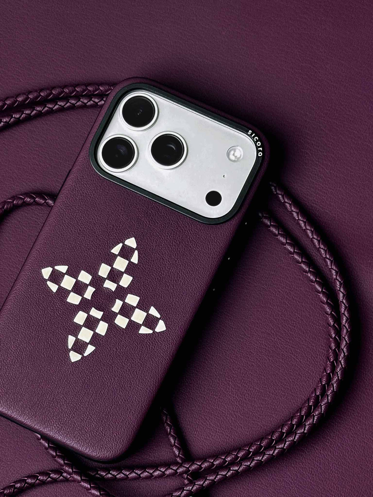 sicora iPhone 18 pro / iPhone 17 pro vegan leather phone case, bloom case featuring handcrafted cream white color blocking petal pattern on a cherry purple premium SILIO silicone vegan leather, braided phone lanyards and purple leather backdrop.