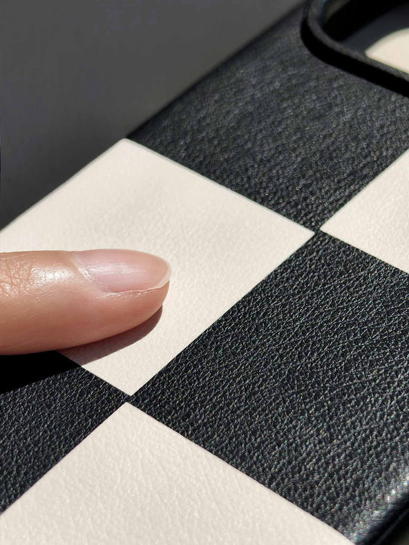 Close-up of a sicora black and cream-white checkered leather marquetry patterned iPhone 18 pro / iPhone 17 pro case macro case with a finger touching the textured surface