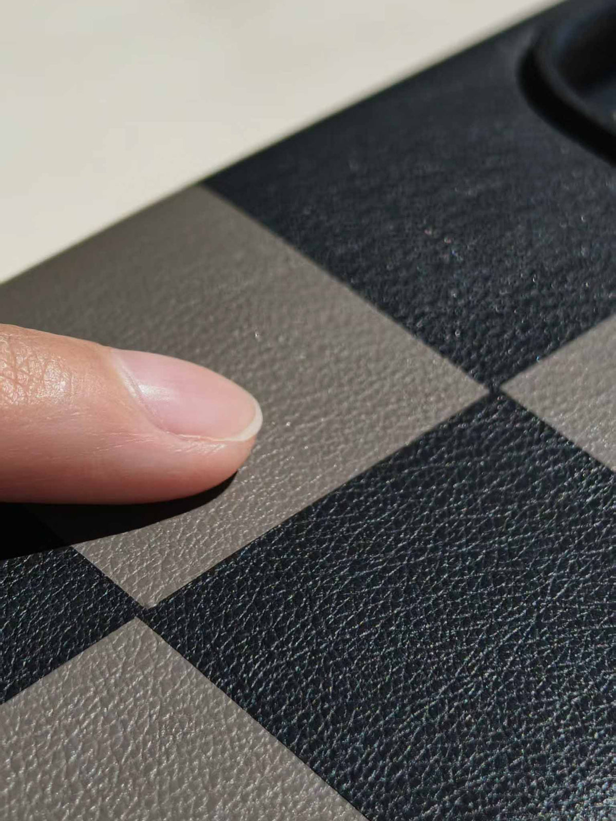 Close-up of a finger touching a sicora black and gray checkered textured leather marquetry iPhone 18 pro / iPhone 17 pro case, macro case.