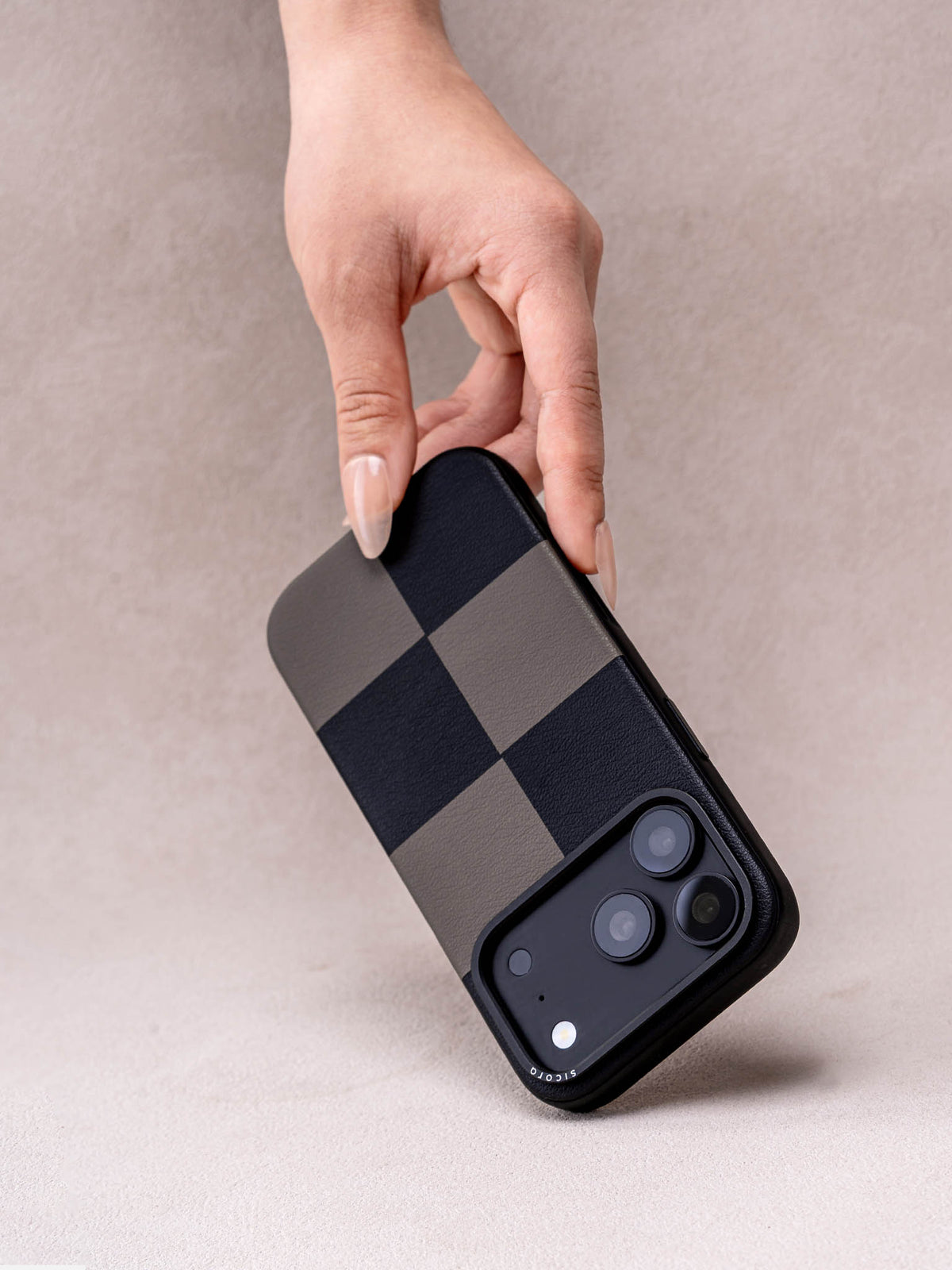 Hand holding a sicora iPhone 18 pro / iPhone 17 pro vegan leather phone case, macro case featuring a black and gray checkered leather marquetry pattern