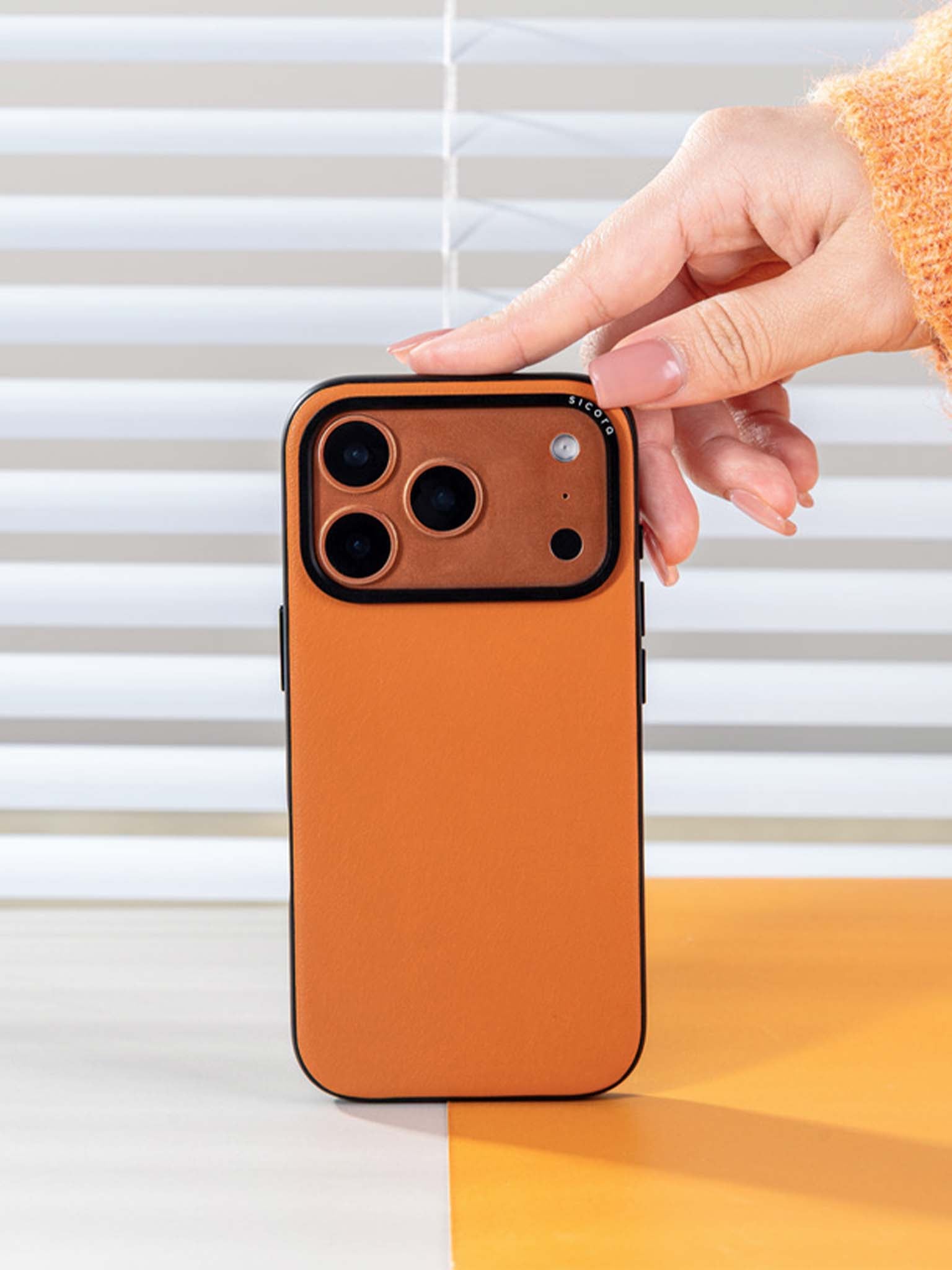 A hand touching a toffee gold sicora moodblock phone case with silio silicone vegan leather