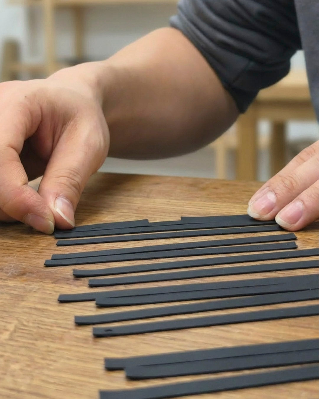 A craftsman arranging black silicone leather strips on a wooden surface