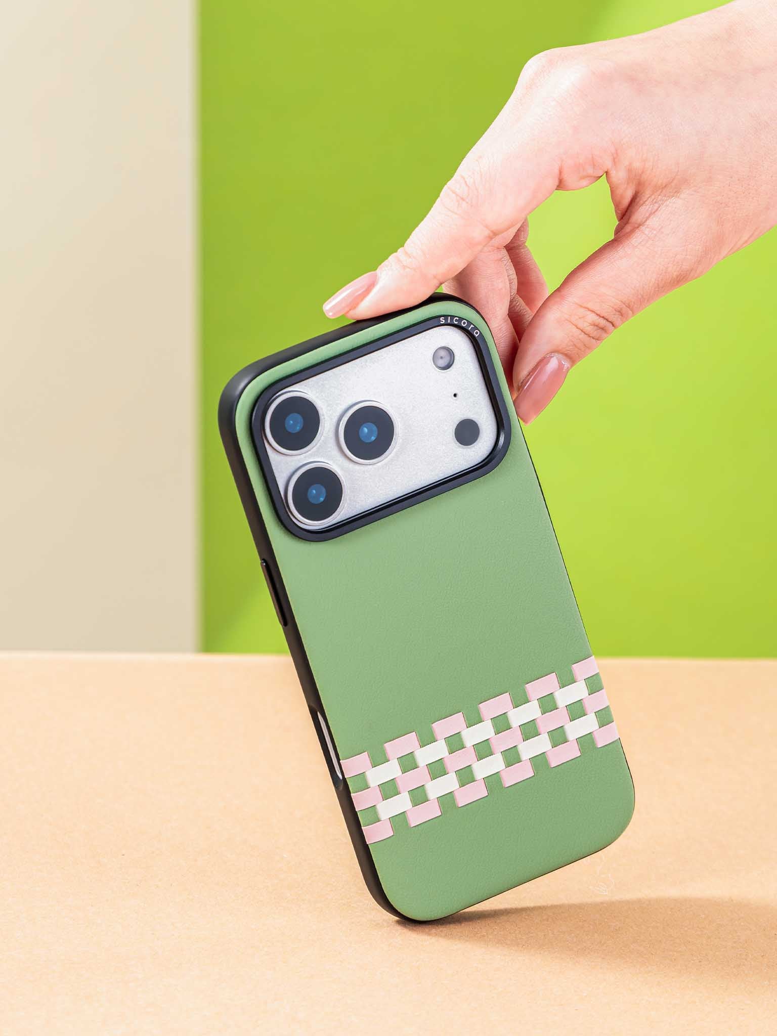 Sicora stitchon phone case with avocado green, pink and cream white geometric pattern held by a hand against a colorful background