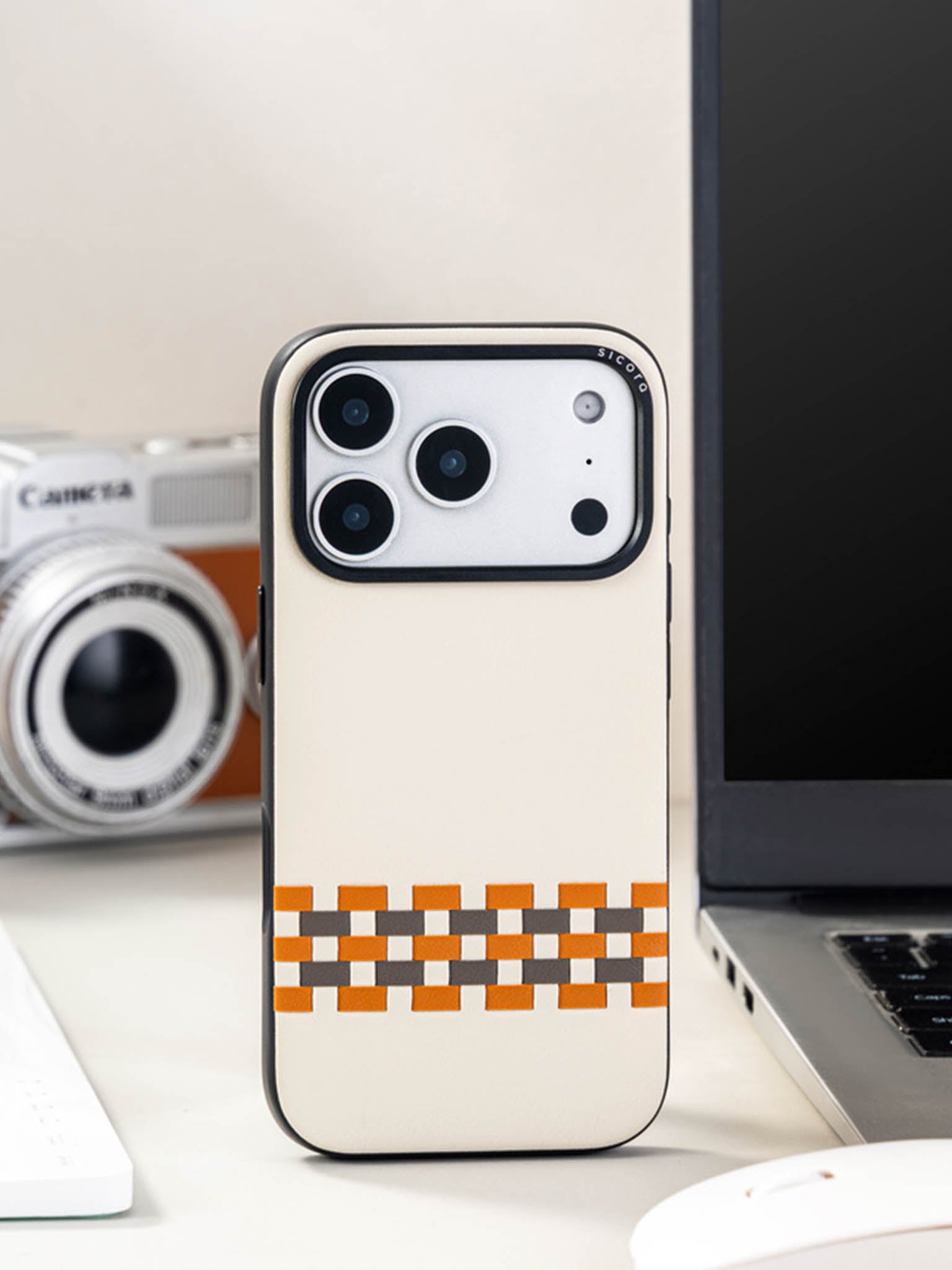 Sicora stitchon phone case with cream white, toffee gold and granite gray geometric pattern on a desk with camera and laptop in the background