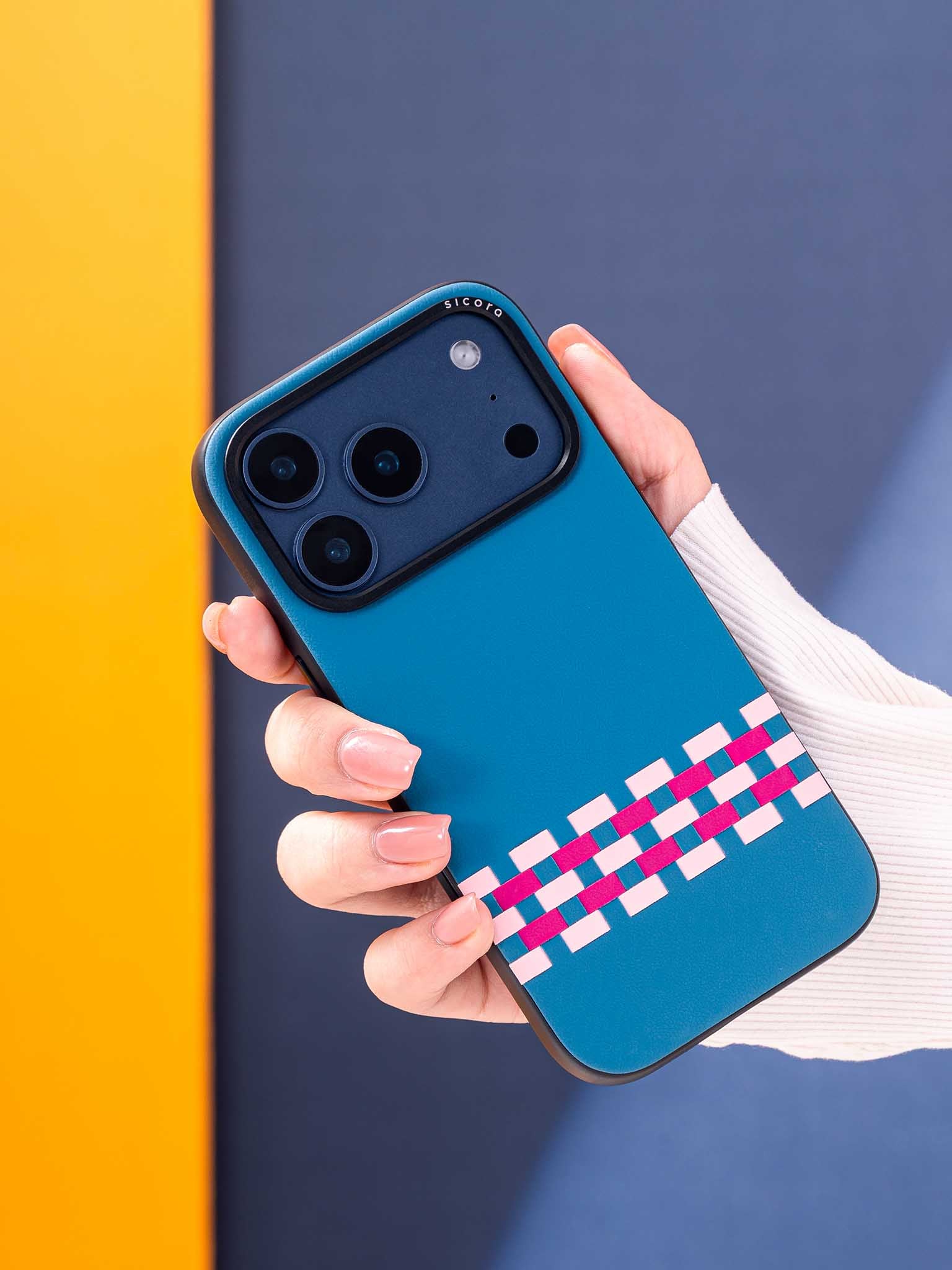 Hand holding a sicora stitchon phone case with sea blue, pink and magenta geometric pattern against a colorful background