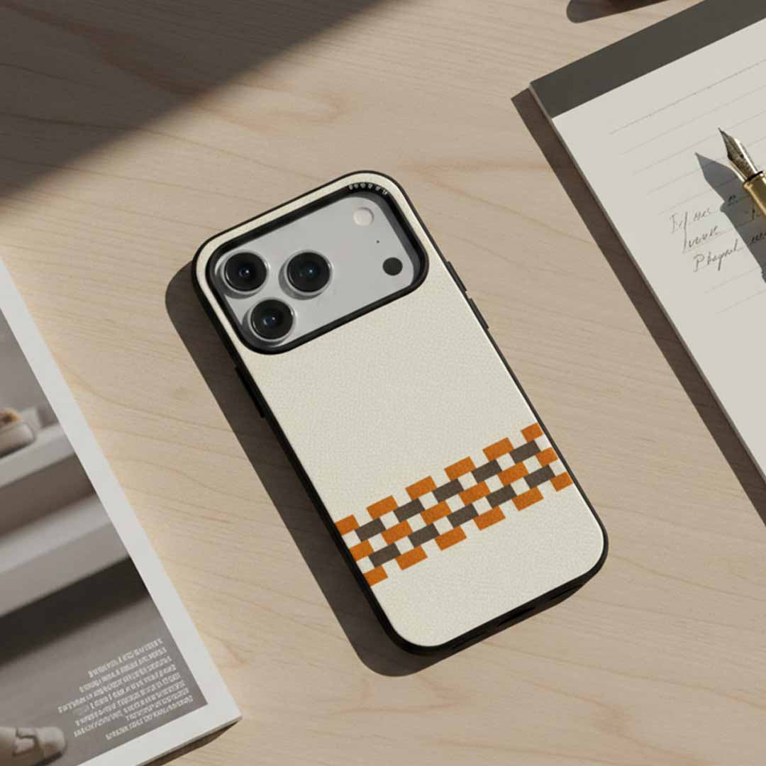 A sicora stitchon iPhone case in silio silicone vegan leather with cream white, toffee god and granite gray geometric pattern on a wooden writing table