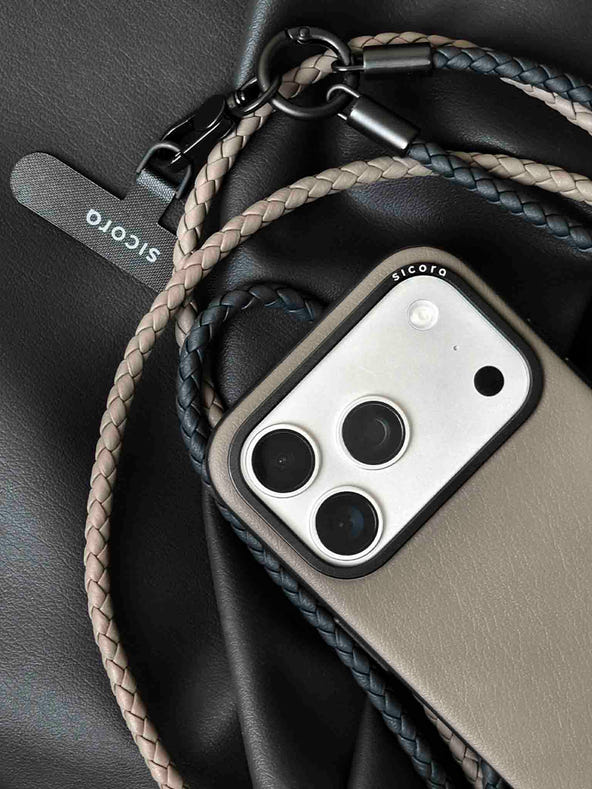 A close-up of a gray sicora moodblock iPhone 17 pro case with braided lanyards and black carabiner.