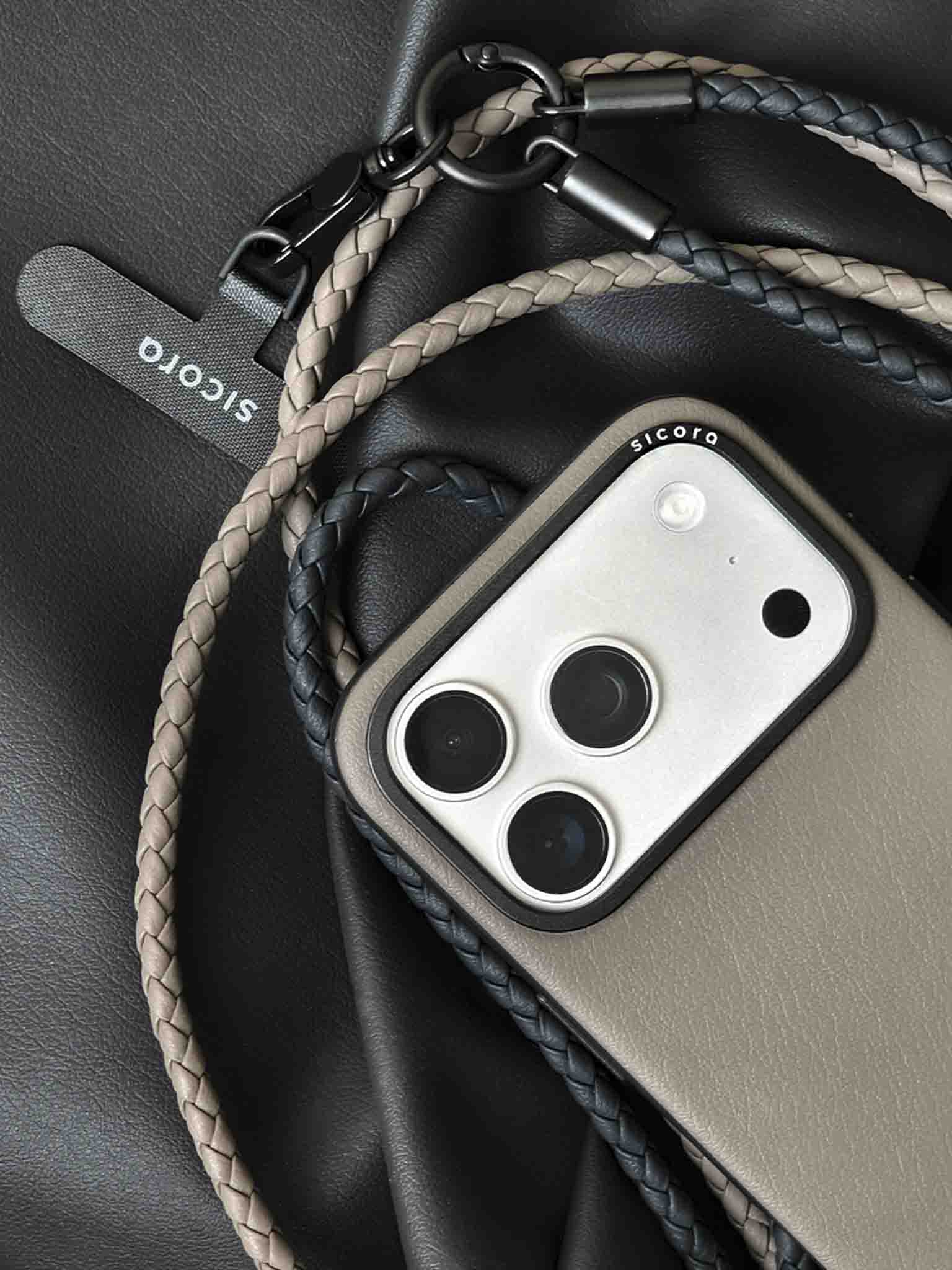 A close-up of a gray sicora moodblock iPhone 17 pro case with braided lanyards and black carabiner.