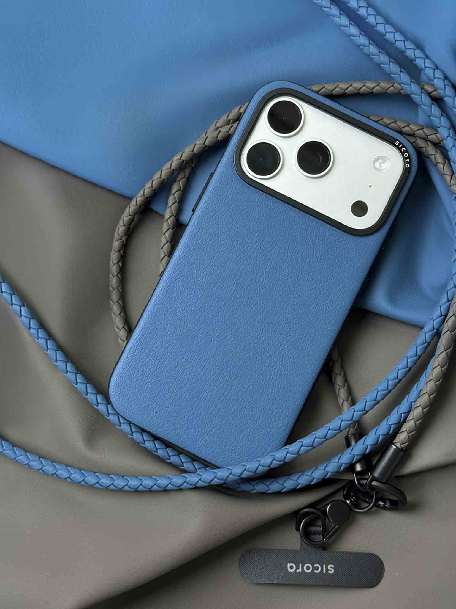 A blue sicora moodblock iPhone 17 pro case with braided lanyards and black carabiner.