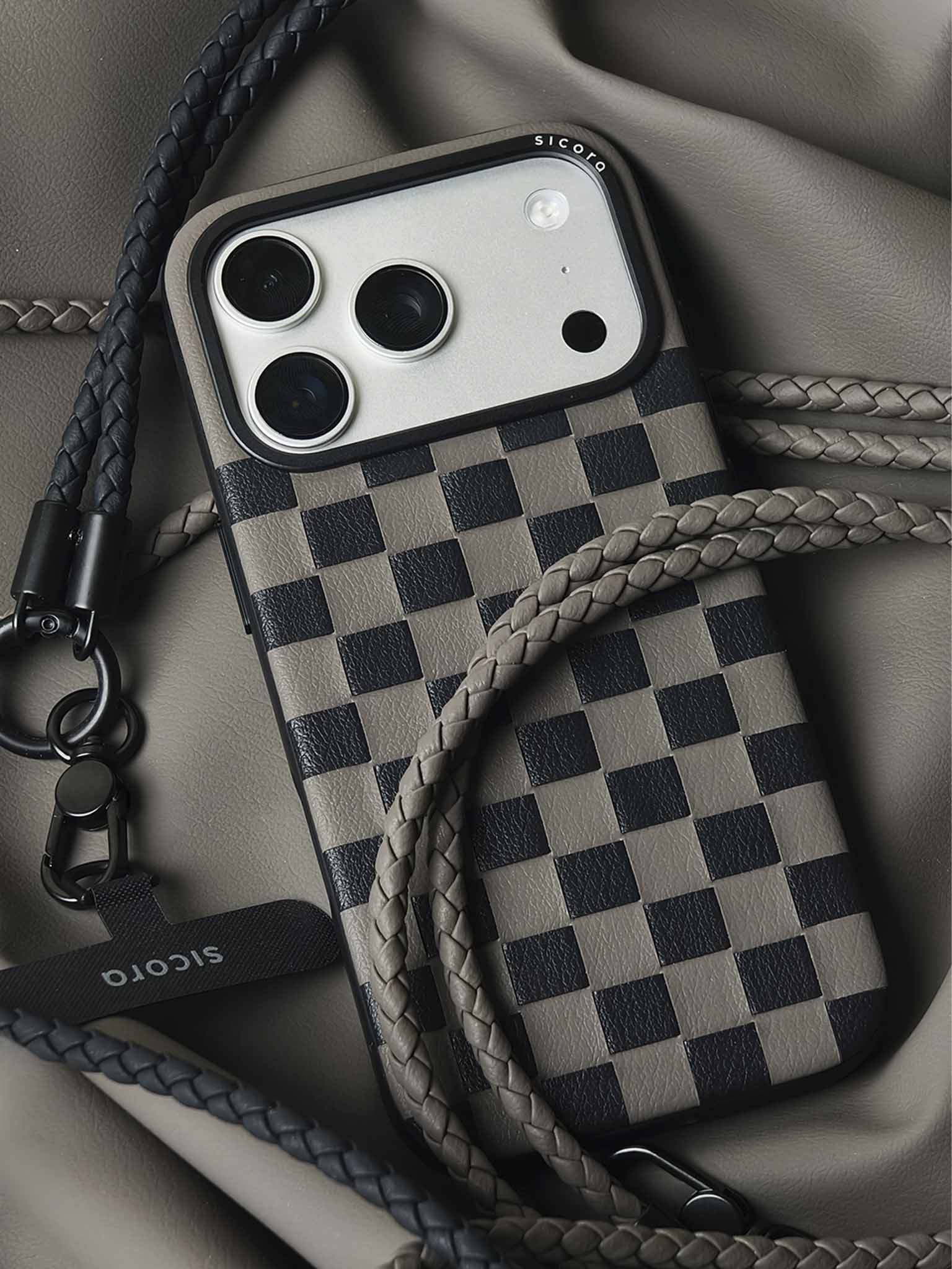 A black gray sicora checkerboard iPhone 17 pro case with braided lanyards and black carabiner.