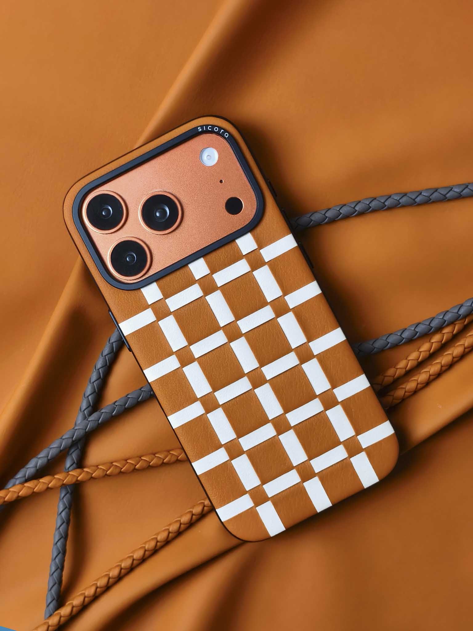 An orange brown sicora gridplay iPhone 17 pro case with braided lanyards and black carabiner.
