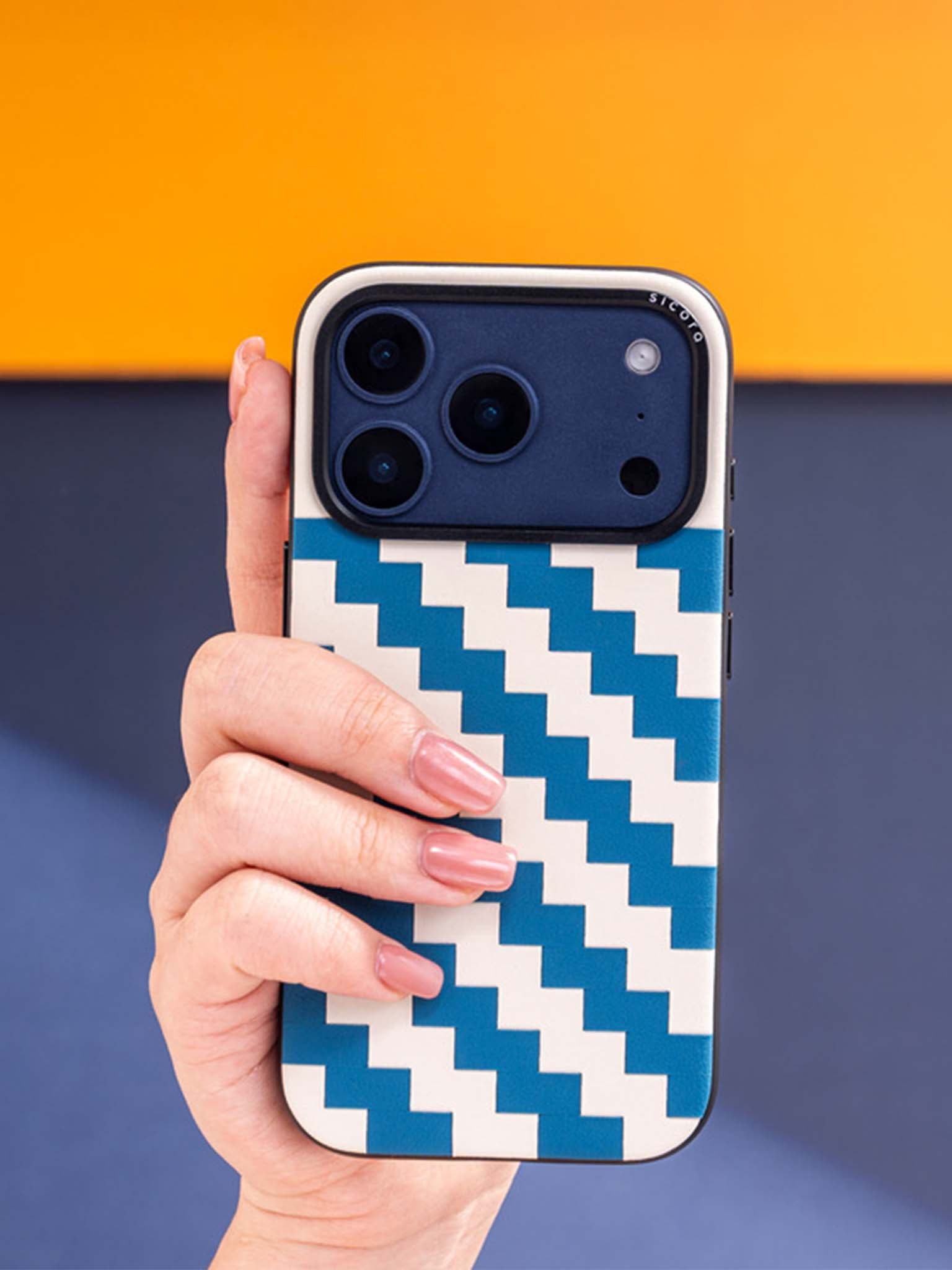 Sicora zigzag phone case with sea blue and cream white zigzag pattern held by a hand against a colorful background